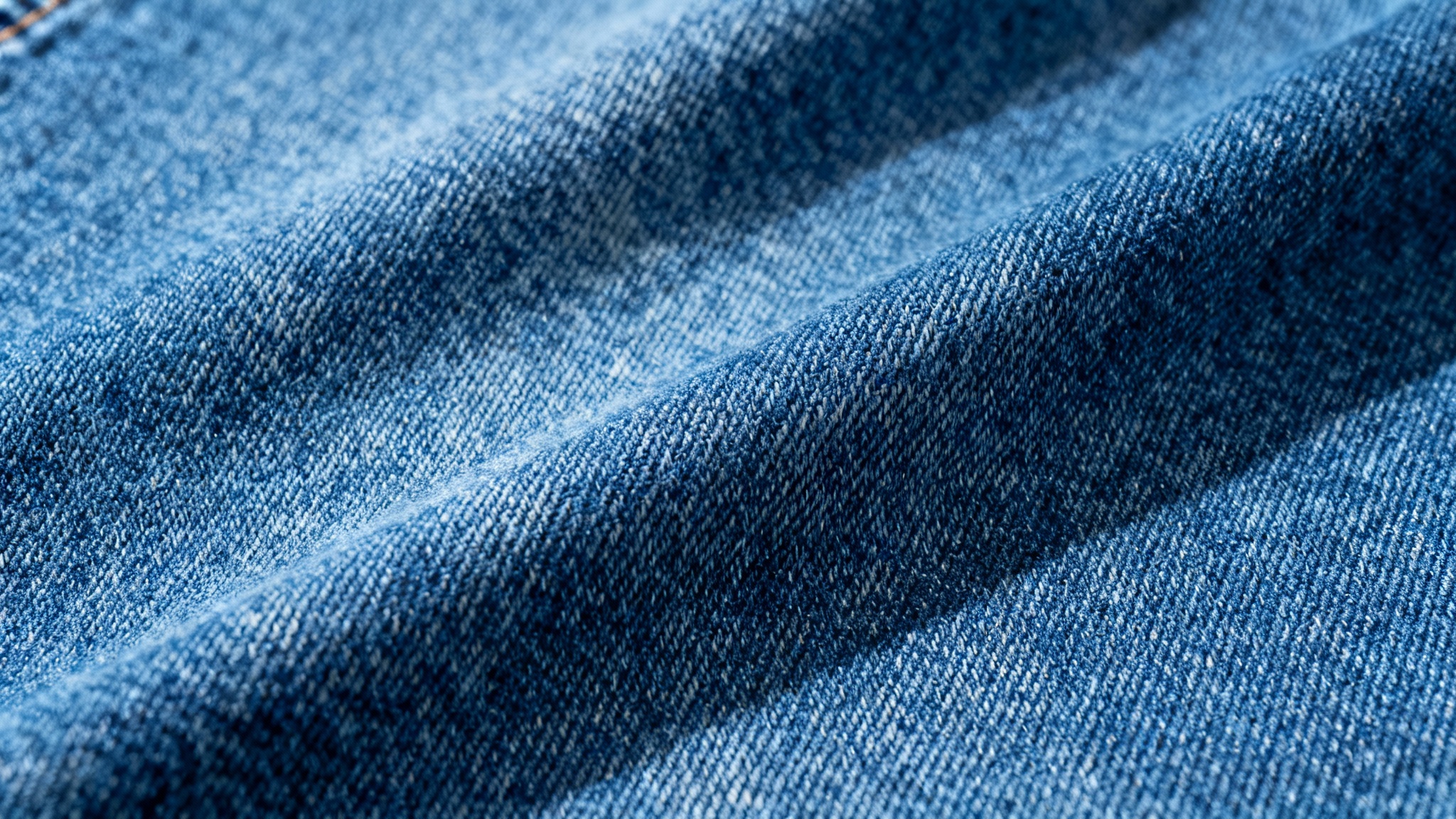 A seamless, high-resolution texture of classic blue denim fabric, shown in a detailed close-up that highlights the diagonal twill weave.