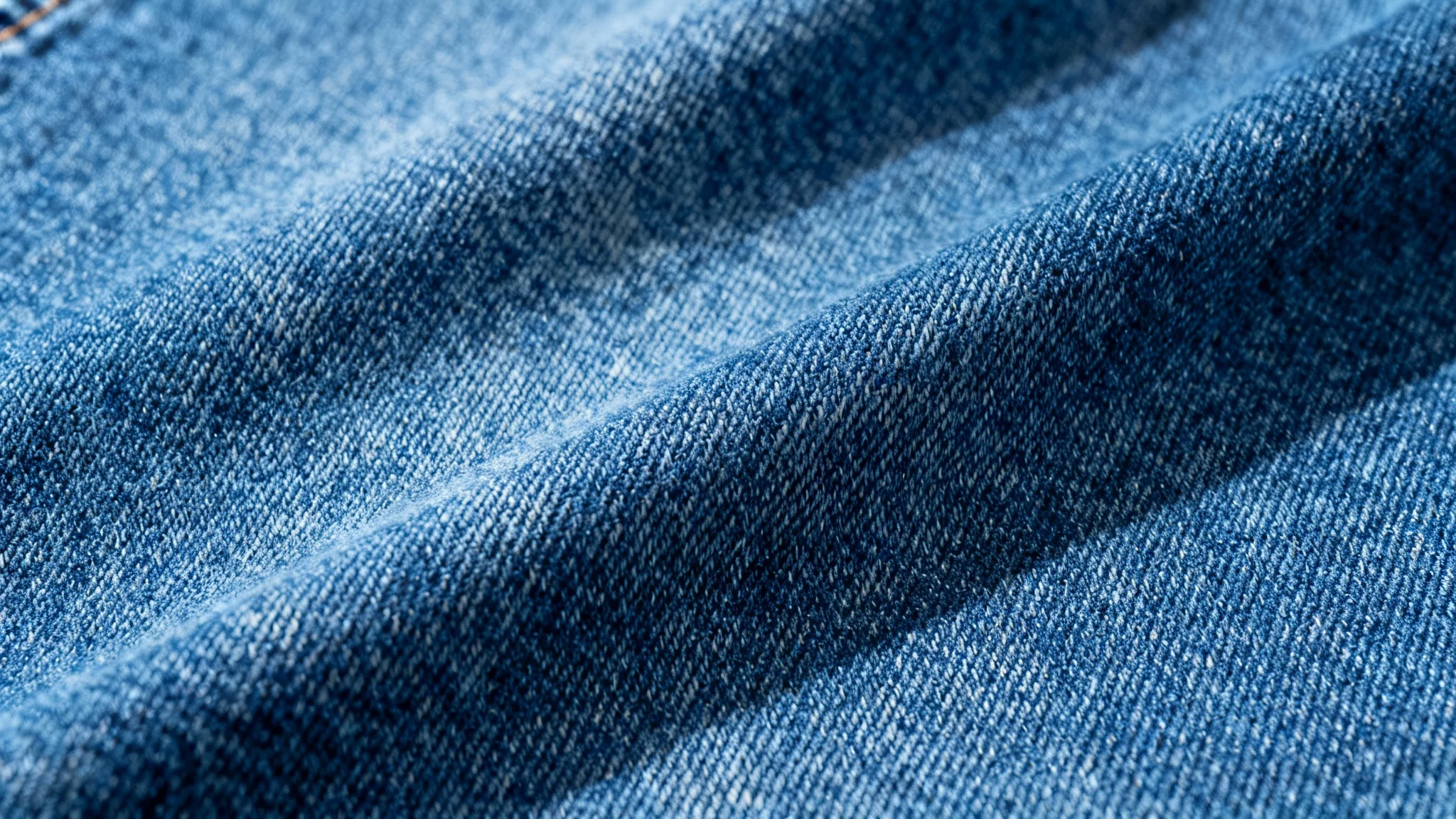 A seamless, high-resolution texture of classic blue denim fabric, shown in a detailed close-up that highlights the diagonal twill weave.