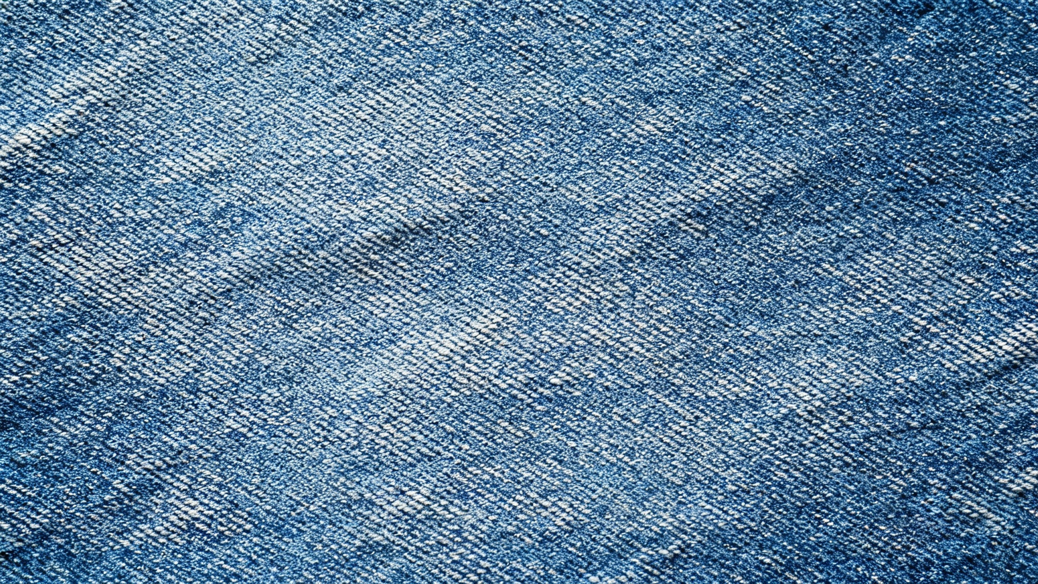 A high-resolution, top-down macro shot of a seamless blue denim texture, showing the detailed diagonal weave of the fabric.