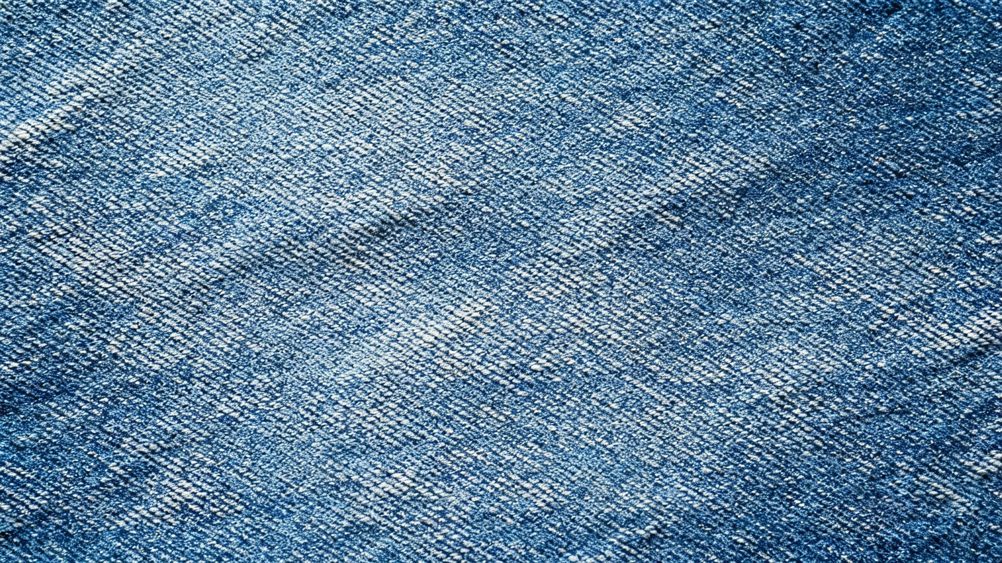 A high-resolution, top-down macro shot of a seamless blue denim texture, showing the detailed diagonal weave of the fabric.