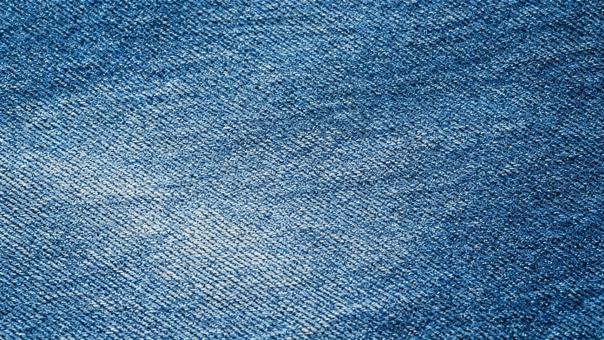 A high-resolution, top-down image of a seamless blue denim texture, showcasing the detailed diagonal weave and fabric threads.