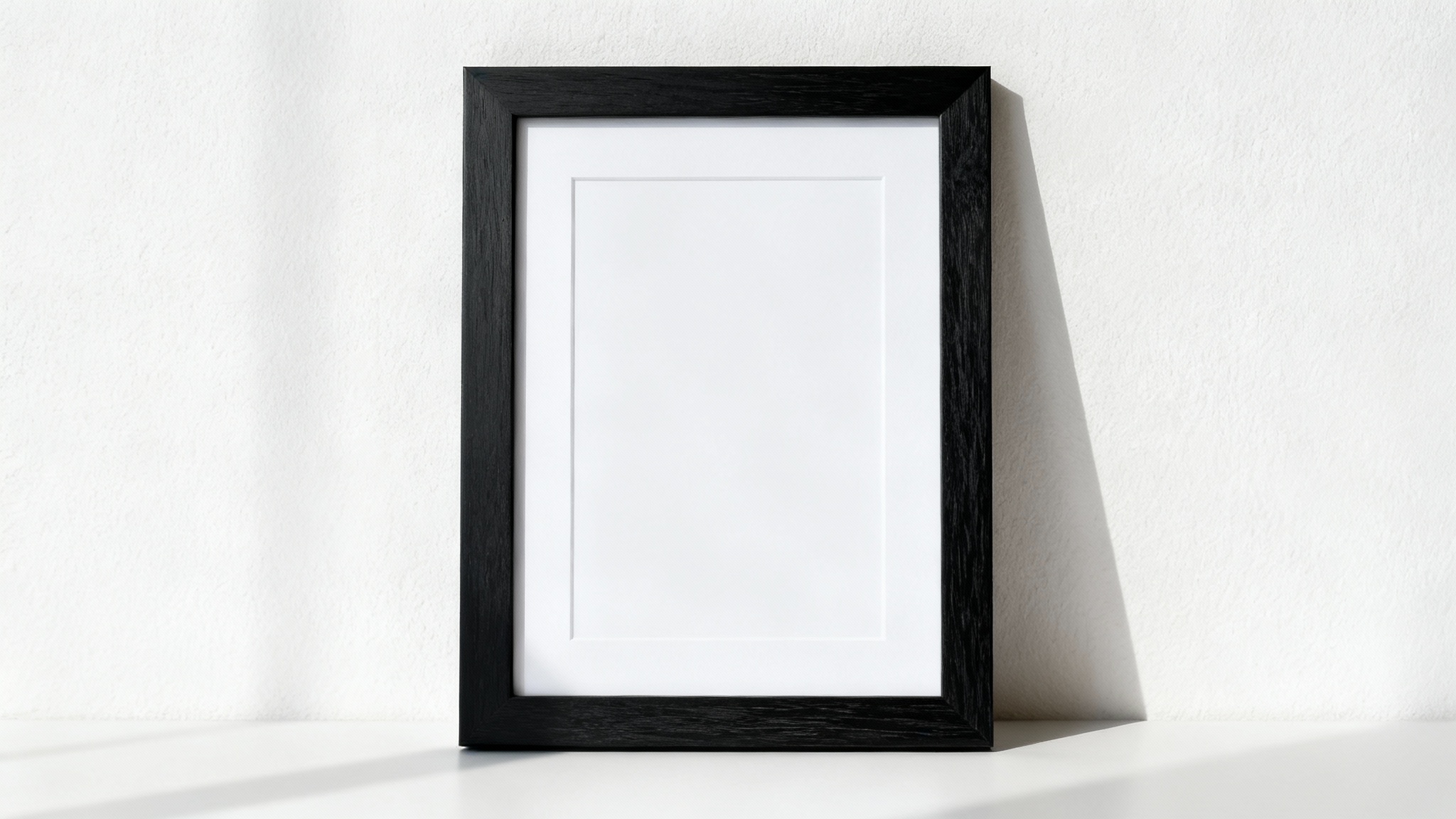 A professional mockup of a single, vertical black wooden frame with a white mat, hanging on a clean, off-white wall in a brightly lit space.