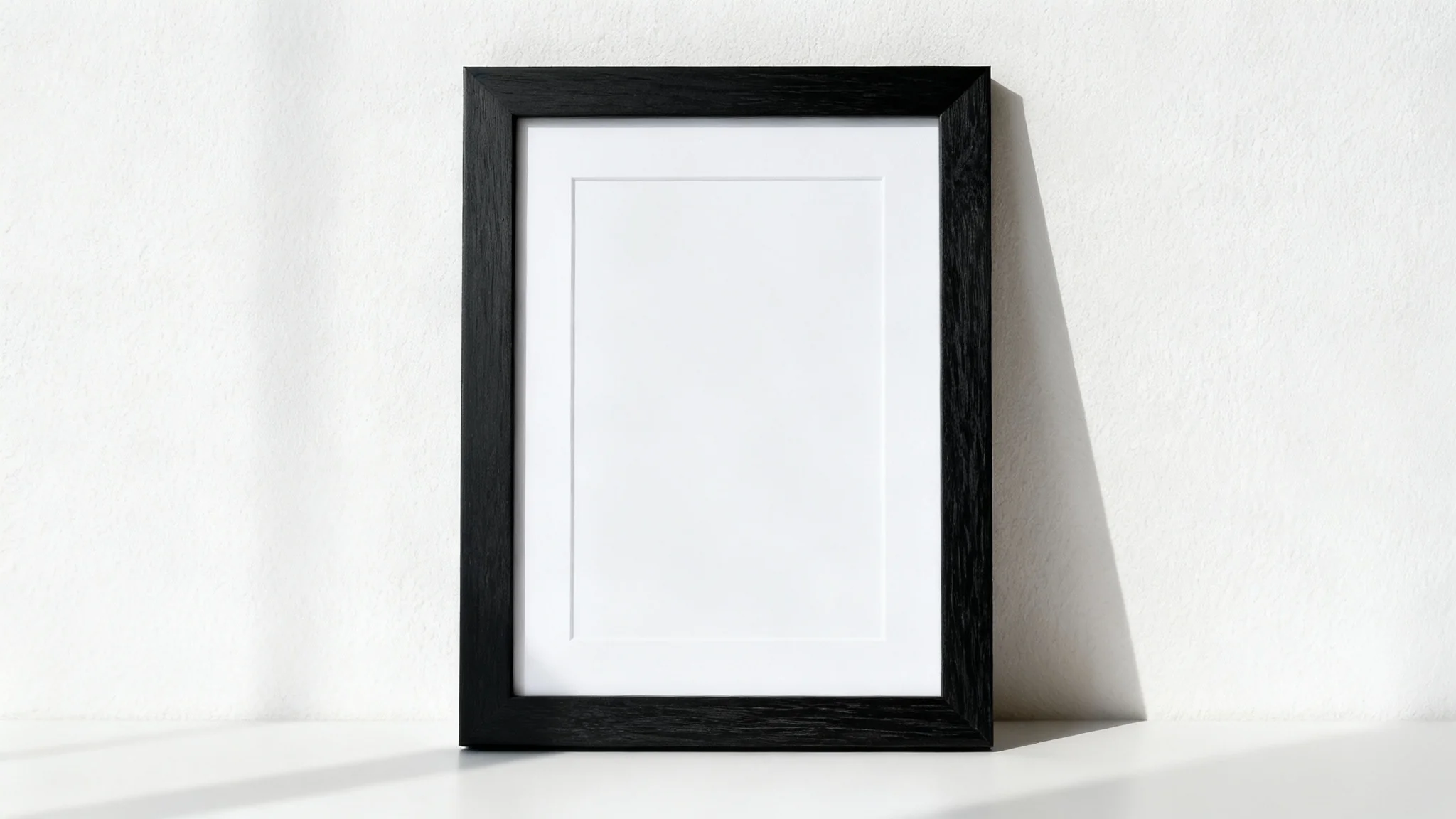 A professional mockup of a single, vertical black wooden frame with a white mat, hanging on a clean, off-white wall in a brightly lit space.