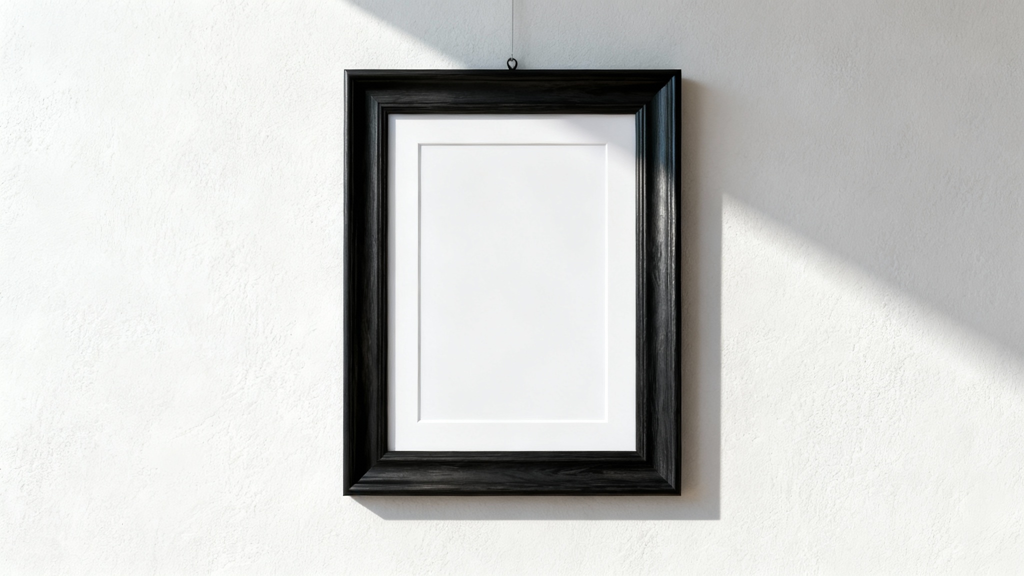 A close-up, front-facing view of a single black wooden picture frame with white matting, hanging on a plain off-white wall in a brightly lit room.