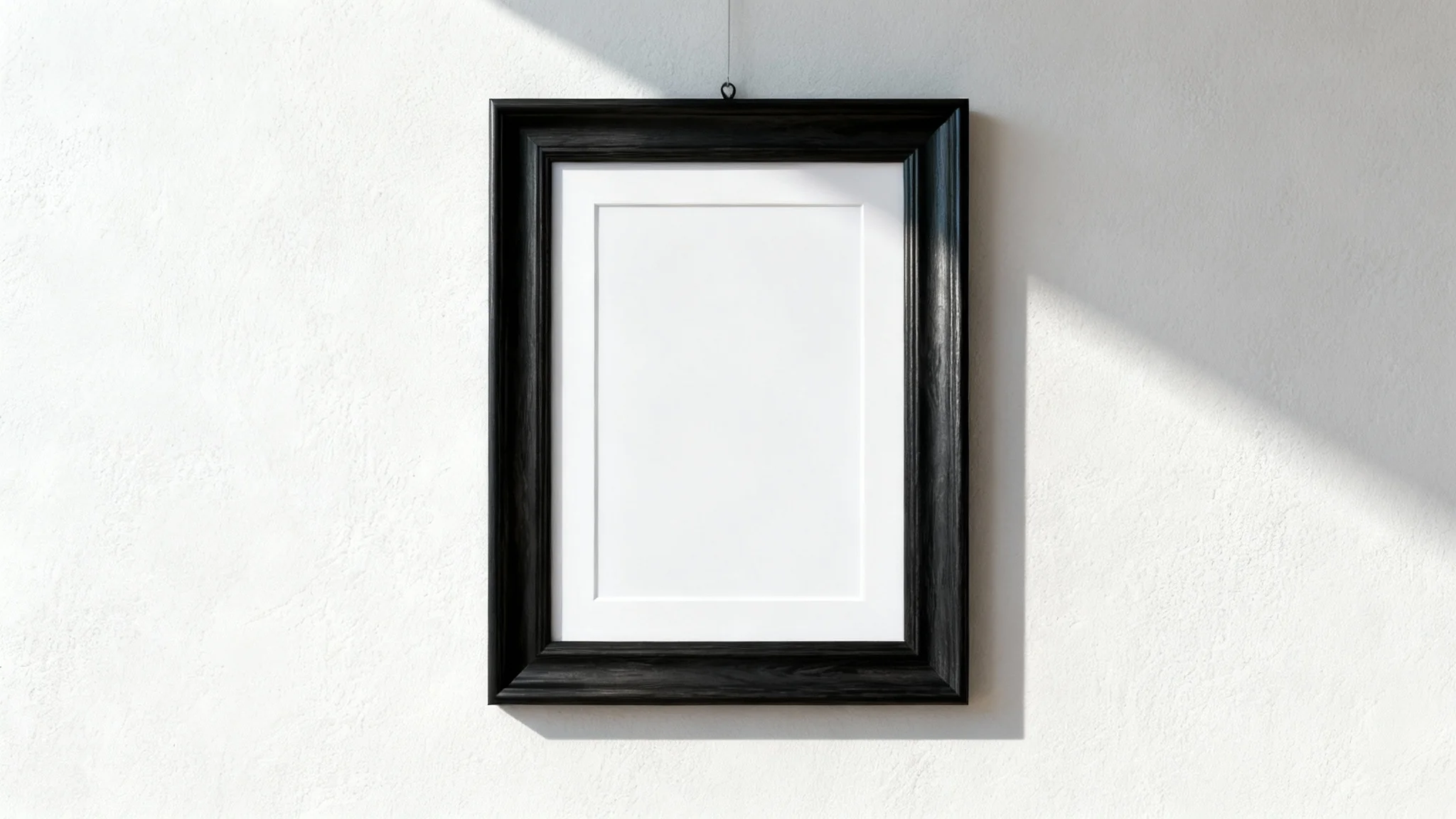 A close-up, front-facing view of a single black wooden picture frame with white matting, hanging on a plain off-white wall in a brightly lit room.