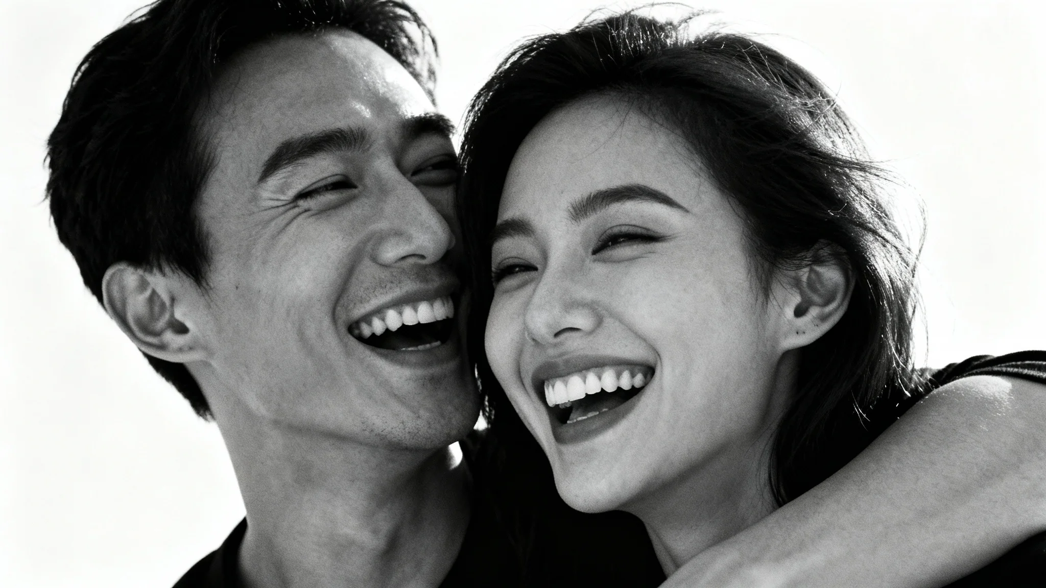 A romantic black and white close-up photo of a young couple laughing together affectionately against a plain white background.