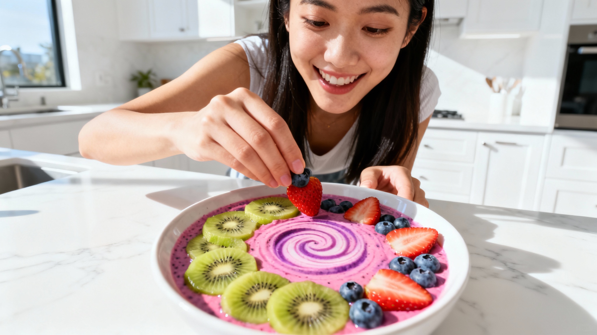 A young woman in a modern white kitchen smiles as she decorates a colorful smoothie bowl with fresh fruit, in a style typical of a popular TikTok cooking video.