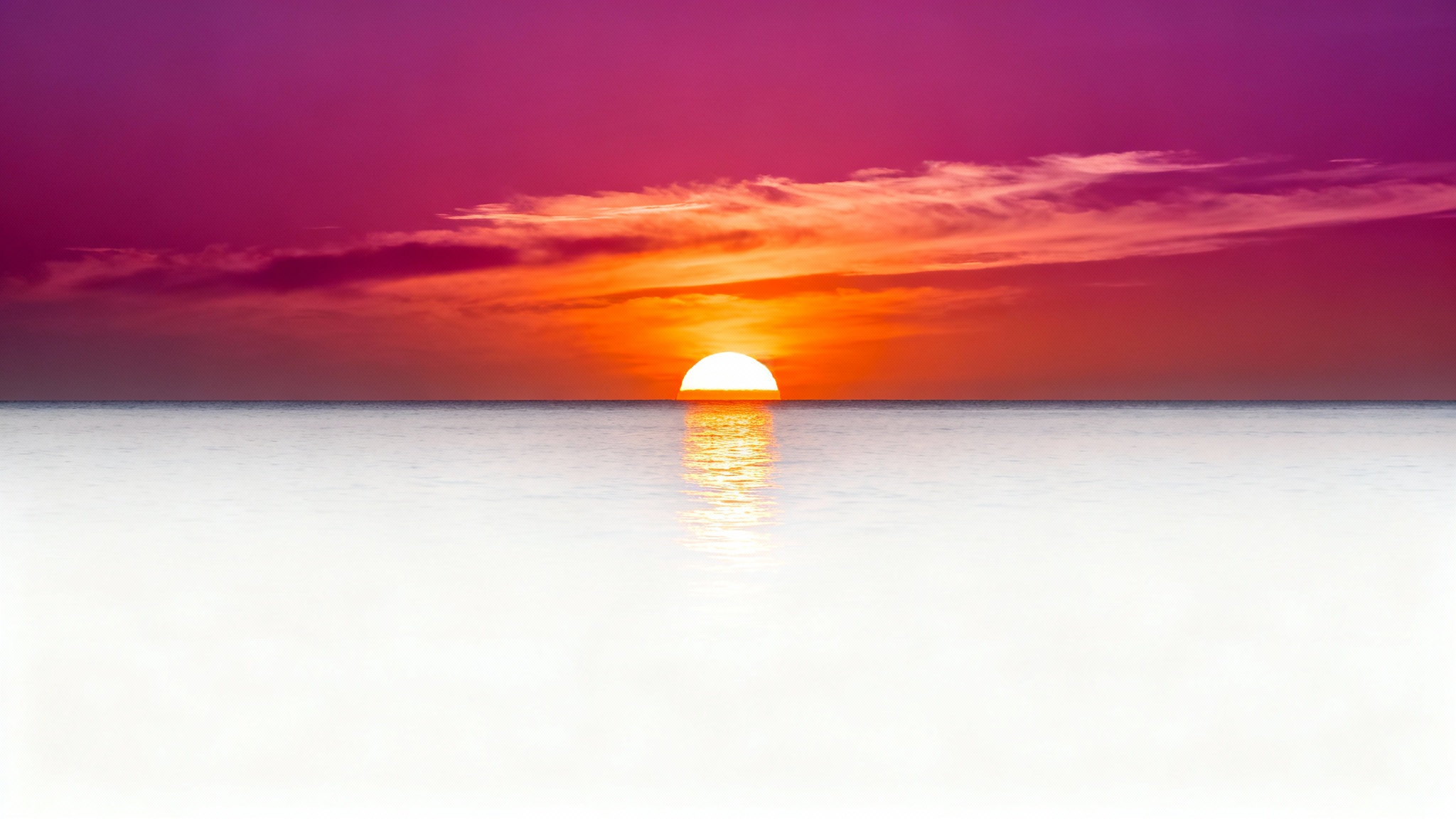 A vibrant and serene sunset over a calm ocean, with the sun dipping below the horizon and casting a golden reflection on the water.
