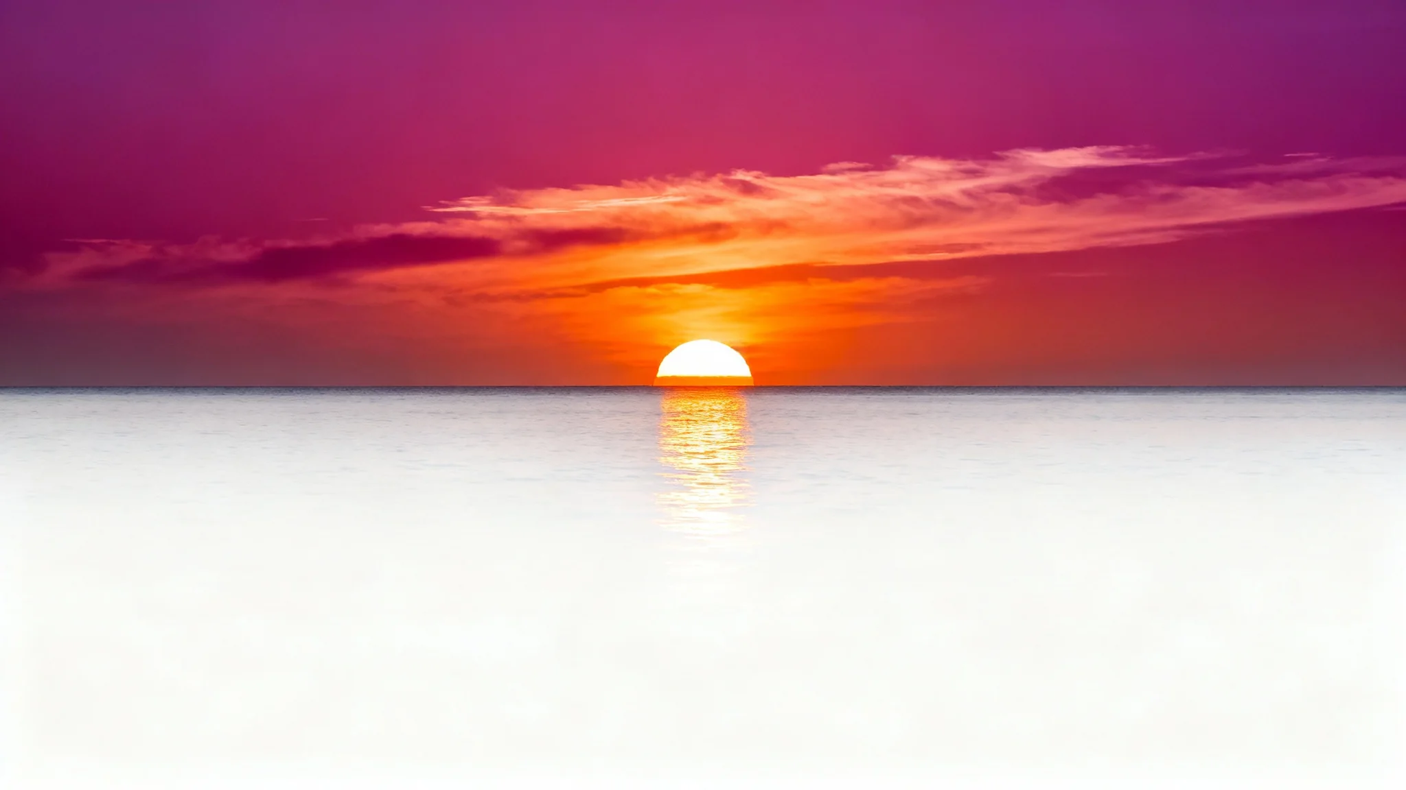 A vibrant and serene sunset over a calm ocean, with the sun dipping below the horizon and casting a golden reflection on the water.